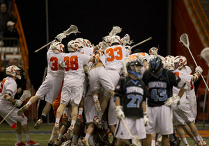 Johns Hopkins players look dejected in foreground as everyone jumps on Stephen Keogh